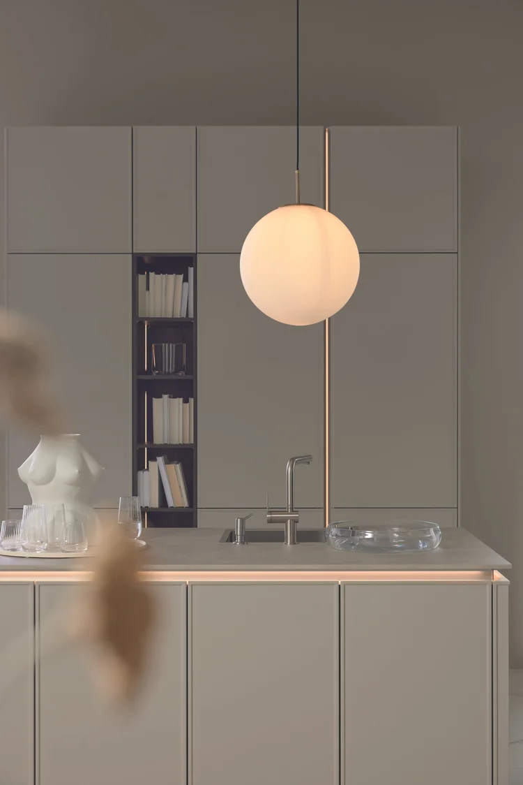 Keukenkasten in zachte greige tint met een ronde hanglamp en een glanzende kraan